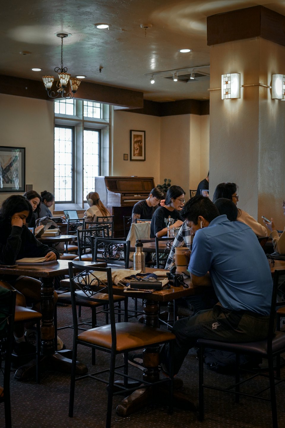 Students work on laptops and books at a wooden table.